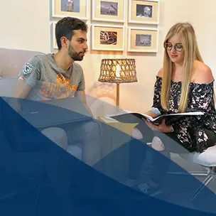 Zwei Personen sitzen mit Laptop und Buch im Schoß, einer schaut auf die andere Person