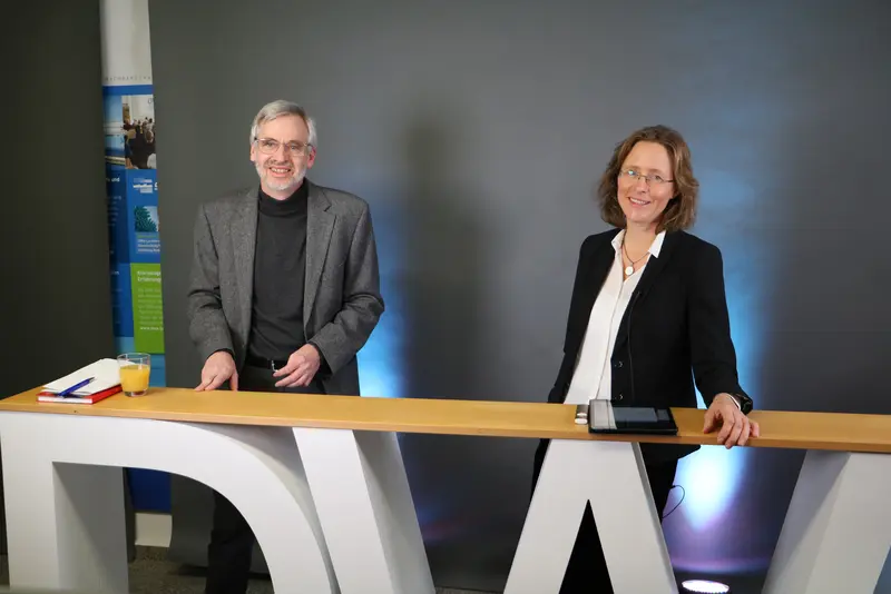 Die Moderatoren Prof. Dr. Peter Baumann und Prof. Dr. Mirijam Gaertner stehen an einer Theke