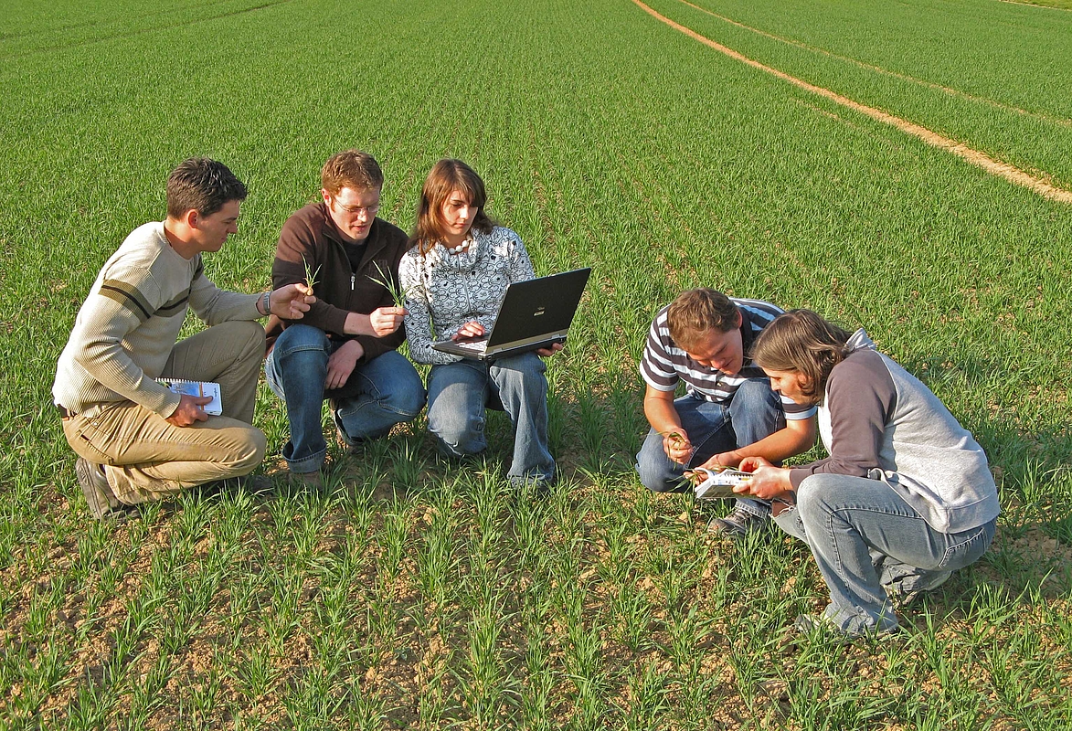 Studierende mit Laptop auf einem Acker
