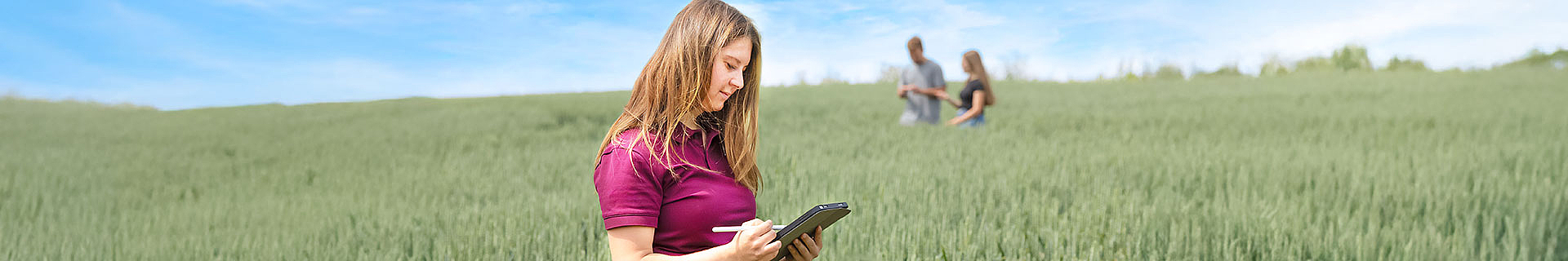 Agribusiness Leitbild mit Studentin mit iPad auf Feld, Horizont mit weiteren Studierenden