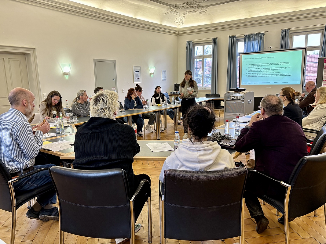 Personen an Tischen, eine Referentin stehend