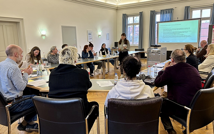 Personen an Tischen, eine Referentin stehend